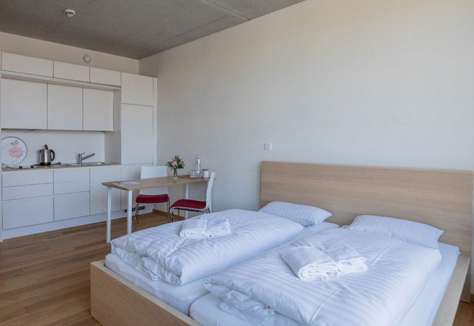 Die Innenansicht eines Apratments im Sukhavati in Bad Saarow zeigt ein Doppelbett mit einer eingebauten Küchenzeile und einen Tisch mit zwei Stühlen