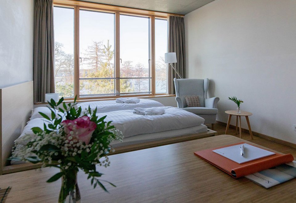 Die Innenansicht des Sukhavati Bad Saarow Apartments zeigt ein Doppelbett und einen Schreibtisch mit Blumen